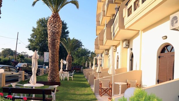 A hotel courtyard with outdoor seating, palm trees, and a pathway leading to the building. - Creta Sun Studios - Adults Only (Chania)