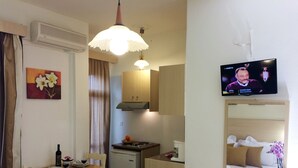 A compact living space with a dining area, kitchenette, and a television displaying a program. - Creta Sun Studios - Adults Only (Chania)