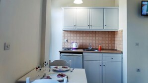 A compact kitchen with white cabinets, a small dining table, and a tiled backsplash. - Creta Sun Studios - Adults Only (Chania)