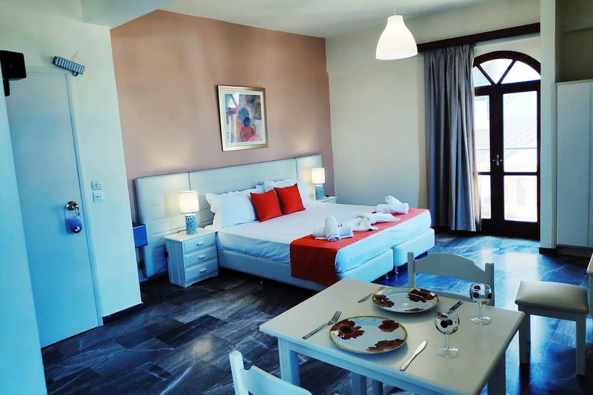 Una habitación de hotel con una cama, mesitas de noche, una mesa de comedor con platos y cubiertos, y una ventana con cortinas.