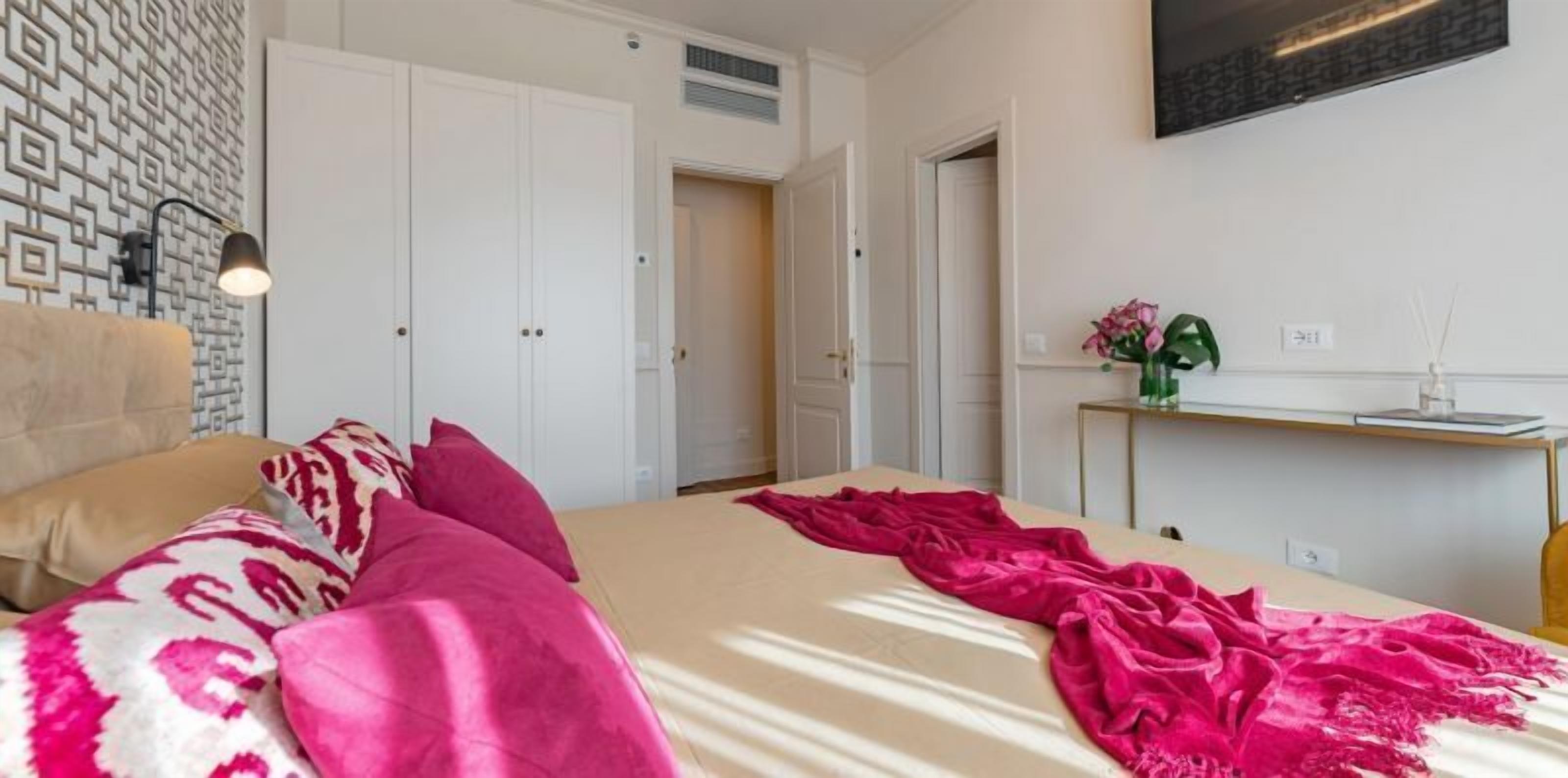 A bedroom with a bed, pillows, a bedside table with a vase of flowers, and a wardrobe.