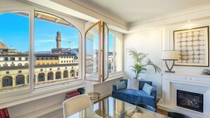 Habitación con un amplio ventanal que ofrece vistas a un edificio histórico con una torre. Hay un sofá azul, una chimenea y una obra de arte enmarcada en la pared.
