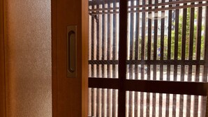 Une vue à travers une grille métallique à barreaux verticaux, donnant sur un espace extérieur doté d’une surface pavée et de verdure.
