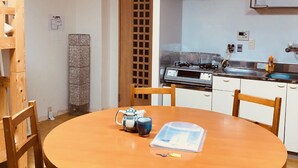 Une cuisine compacte avec des meubles blancs, une cuisinière et un évier. On y trouve une table ronde en bois, des chaises, un petit meuble et un objet décoratif posé sur la table.
