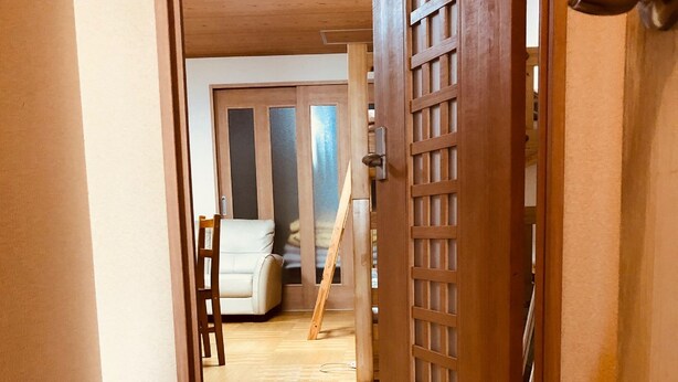 Un couloir intérieur en bois, avec un sol à carreaux, une porte ornée d’un motif traditionnel en treillis et, au fond, un canapé blanc.