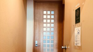 Une porte en bois ornée d’un motif quadrillé, une petite marche menant à cette porte, et deux affiches sur le mur.