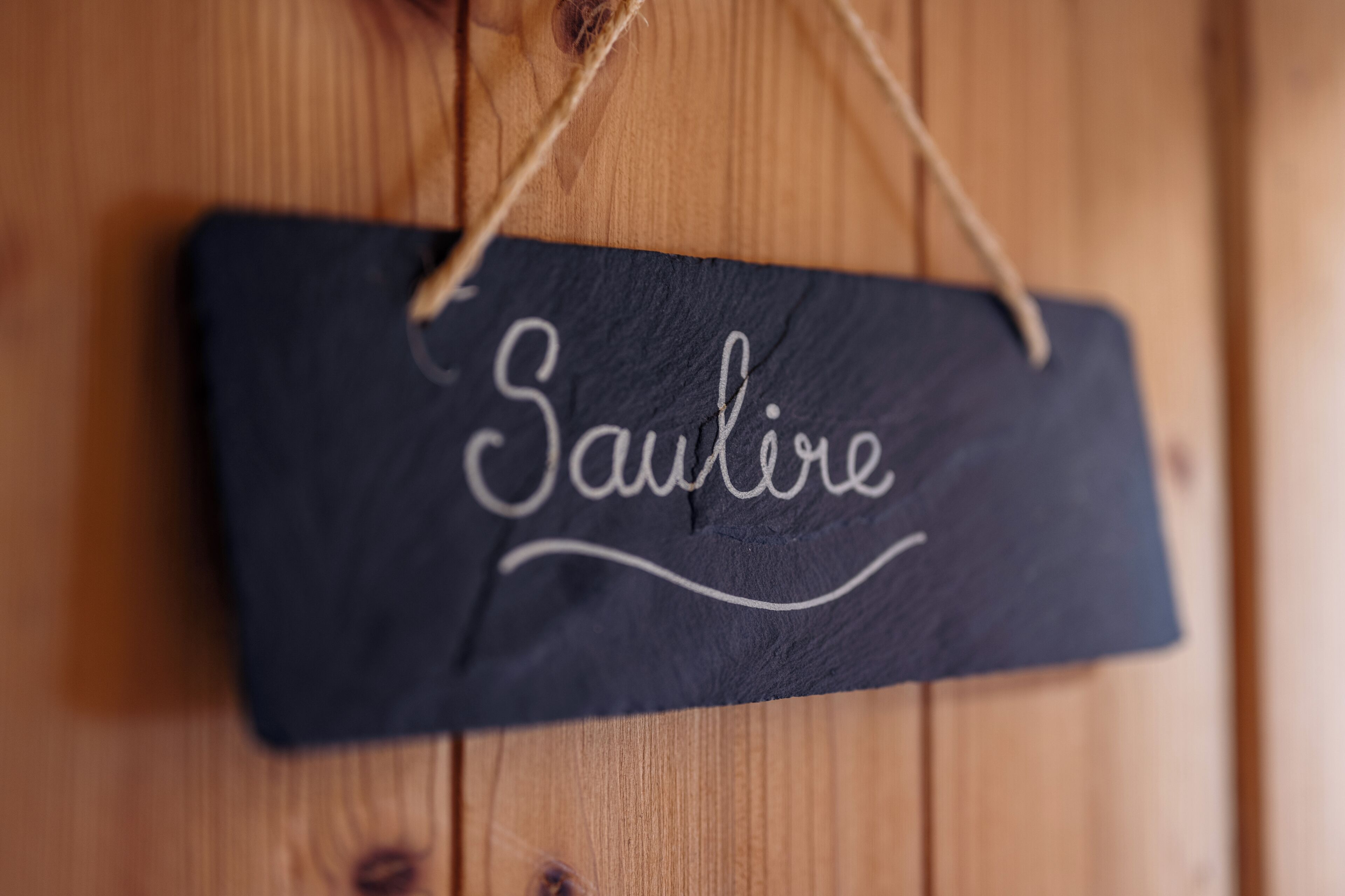 Een grijs bord met de naam 'Saulire' hangt aan een houten muur.