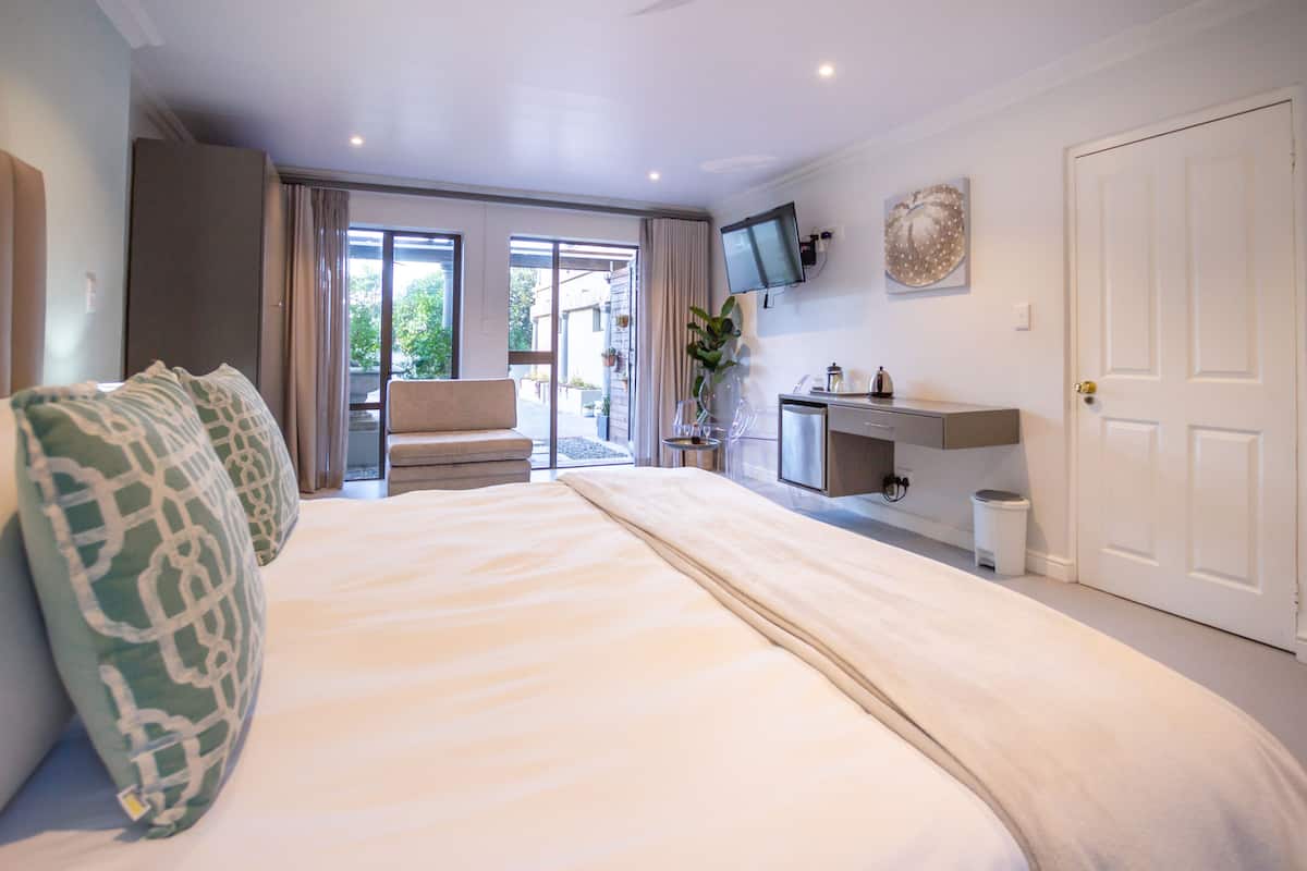 Une chambre d’hôtel moderne dotée d’un grand lit, d’un coin salon avec un canapé et un fauteuil, d’un petit bureau et d’un téléviseur fixé au mur.