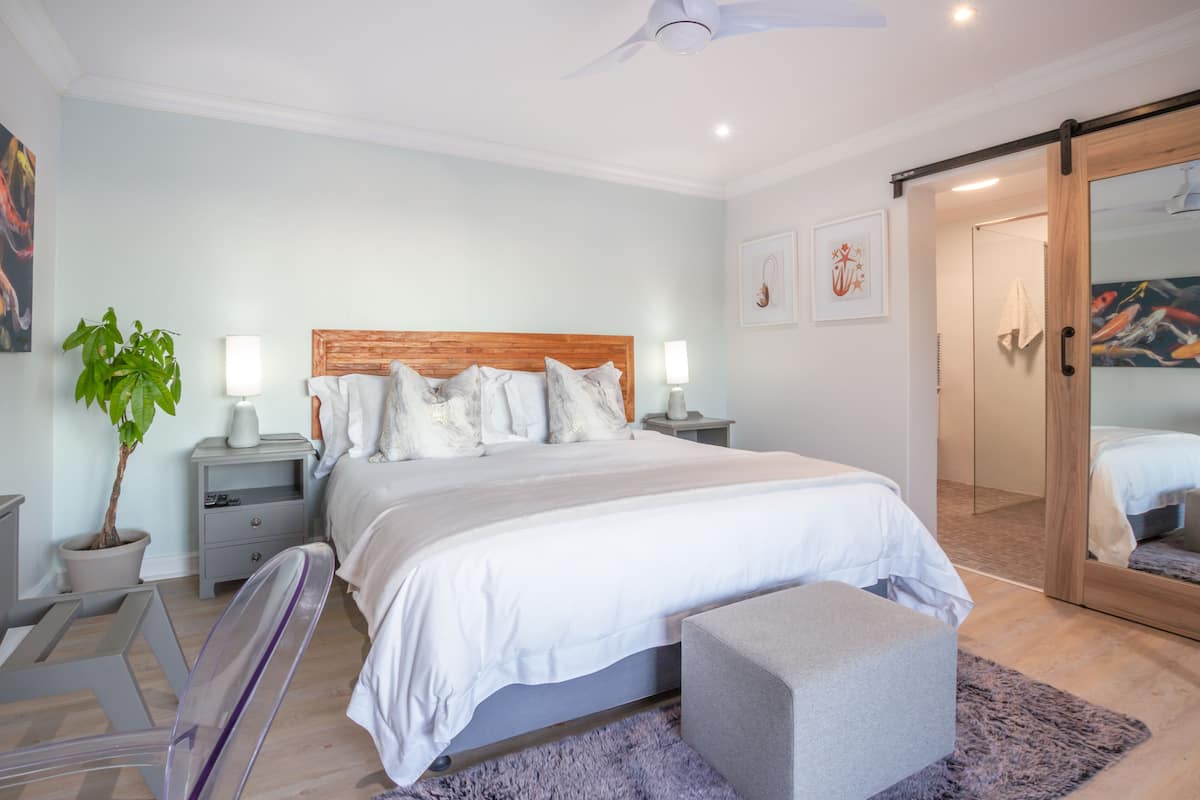 Une chambre moderne avec un grand lit, des tables de chevet, une plante en pot et une porte coulissante donnant accès à une salle de bain.