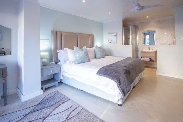 Ein modernes Schlafzimmer mit einem großen Bett, Nachttischen, einem Schminktisch und einem Deckenventilator.