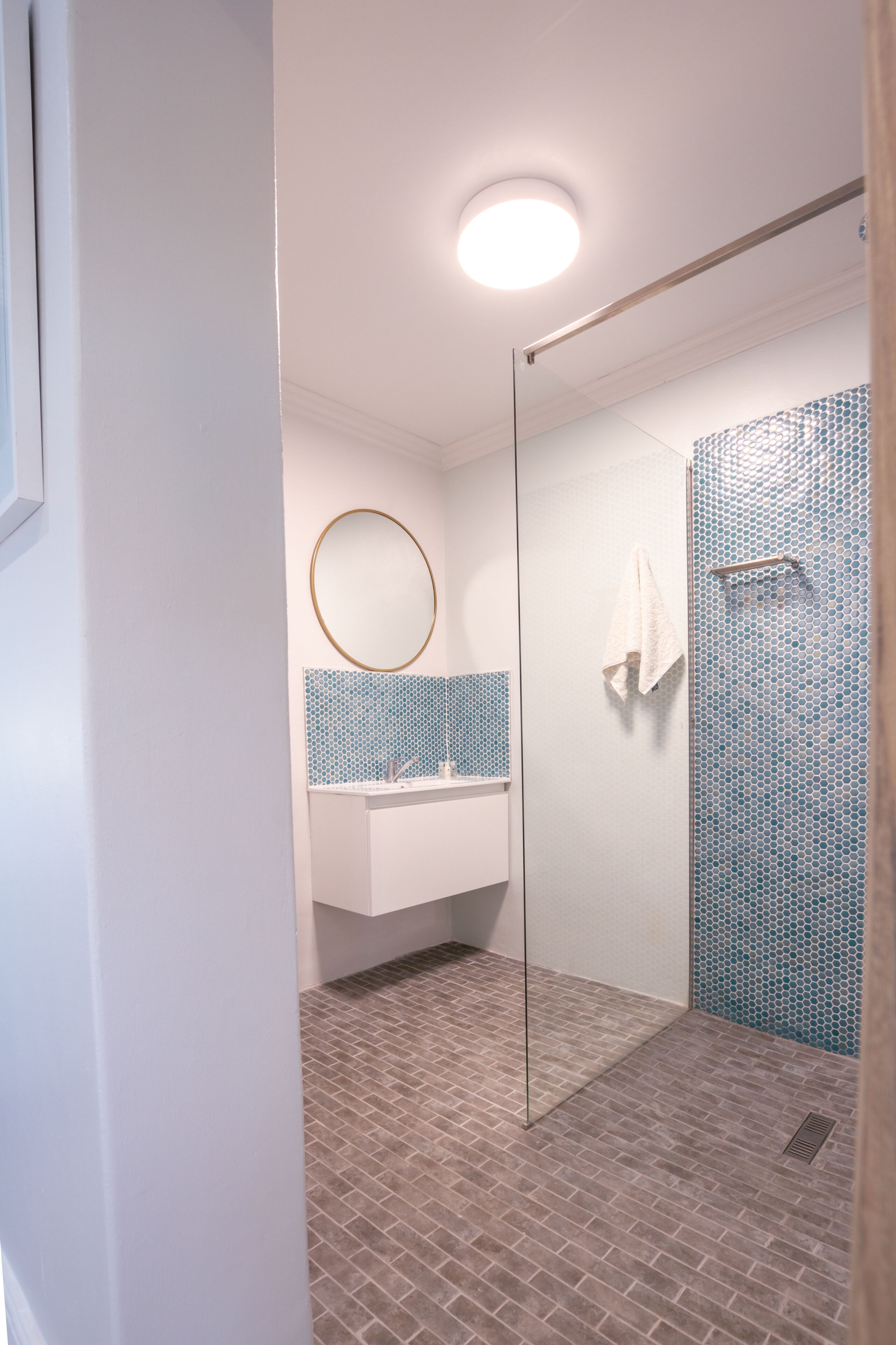 Un baño moderno con cabina de ducha de vidrio, un espejo redondo y un salpicadero de azulejos.
