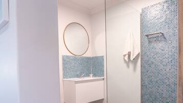 Un baño moderno con cabina de ducha de vidrio, un espejo redondo y un salpicadero de azulejos.
