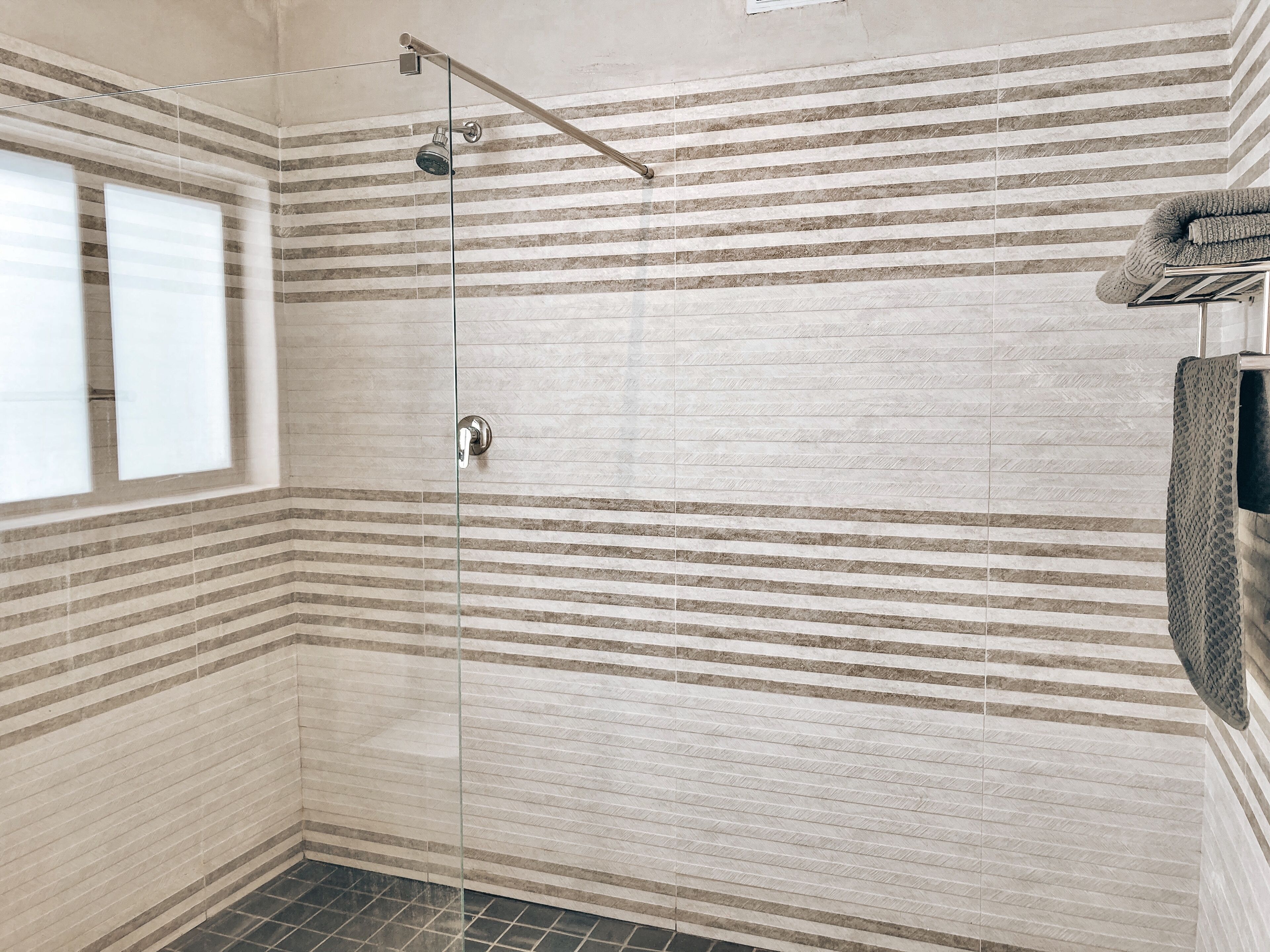 A shower with a glass door, striped wall tiles, and a towel rack with a towel.