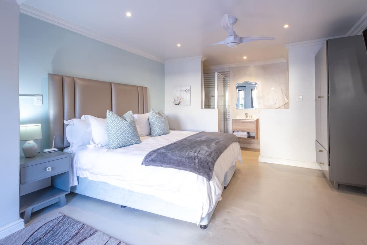 Une chambre moderne avec un grand lit, des tables de chevet, un ventilateur de plafond et un dressing.