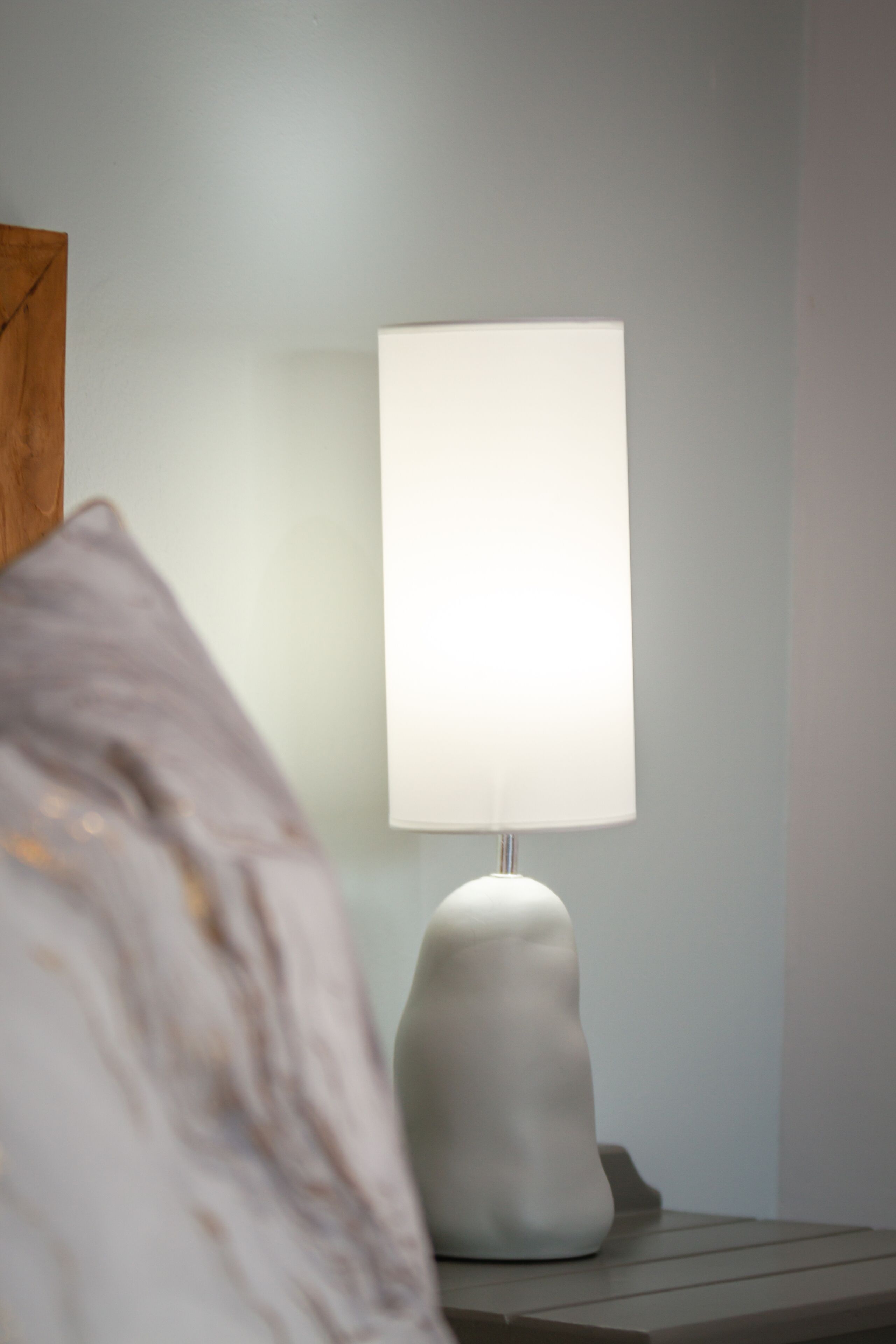 En modern lampa med en vit lampskärm, placerad på ett nattduksbord.