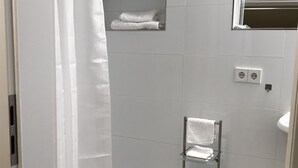 Une salle de bain avec une douche, une étagère en verre où sont posées des serviettes et une petite étagère avec une serviette.