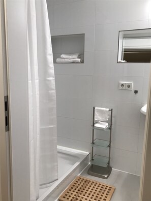 Bathroom features a shower with a glass door and a white curtain, a glass shelf unit, and a small window above.