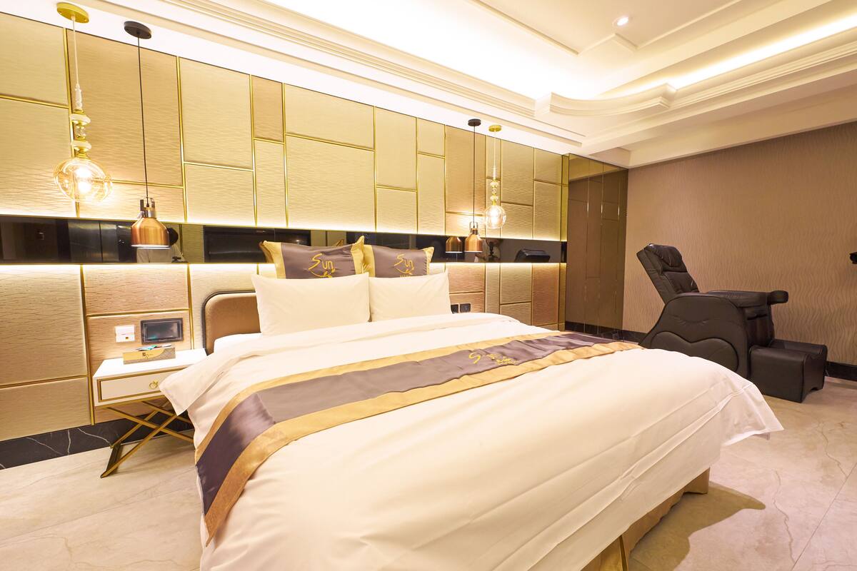 Quarto de hotel moderno com uma cama grande, uma escrivaninha, uma cadeira e um espelho amplo.