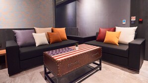 A modern living room with two black sofas, colorful cushions, and a vintage suitcase coffee table with an American flag design. - Sun Motel (Kaohsiung)