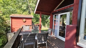 Une terrasse extérieure couverte, aménagée avec des meubles en osier, et un petit bâtiment rouge orné d’une plaque.
