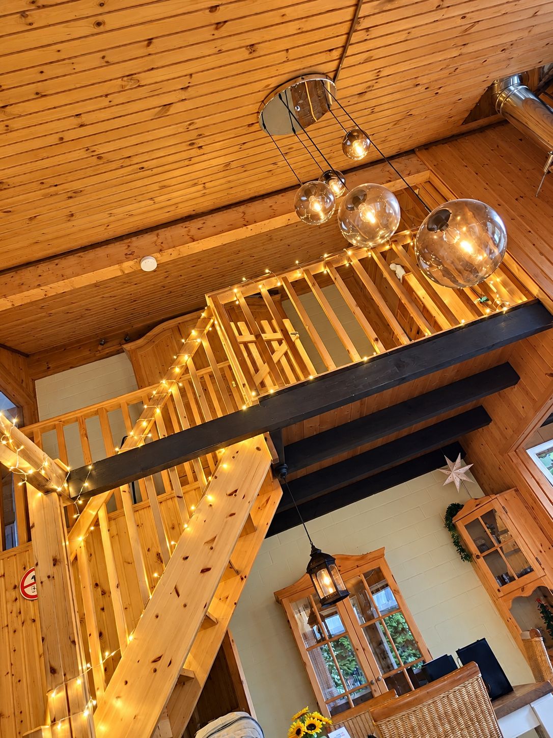 Un intérieur en bois avec un escalier, des guirlandes lumineuses et un luminaire sphérique suspendu.