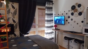Une chambre moderne comprenant un lit, un bureau, deux tabourets de bar, une télévision, une cheminée et des œuvres d’art décoratives au mur.