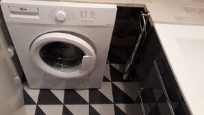 Une machine à laver à chargement frontal se trouve dans une pièce dont le sol est recouvert d’un motif à carreaux noirs et blancs.