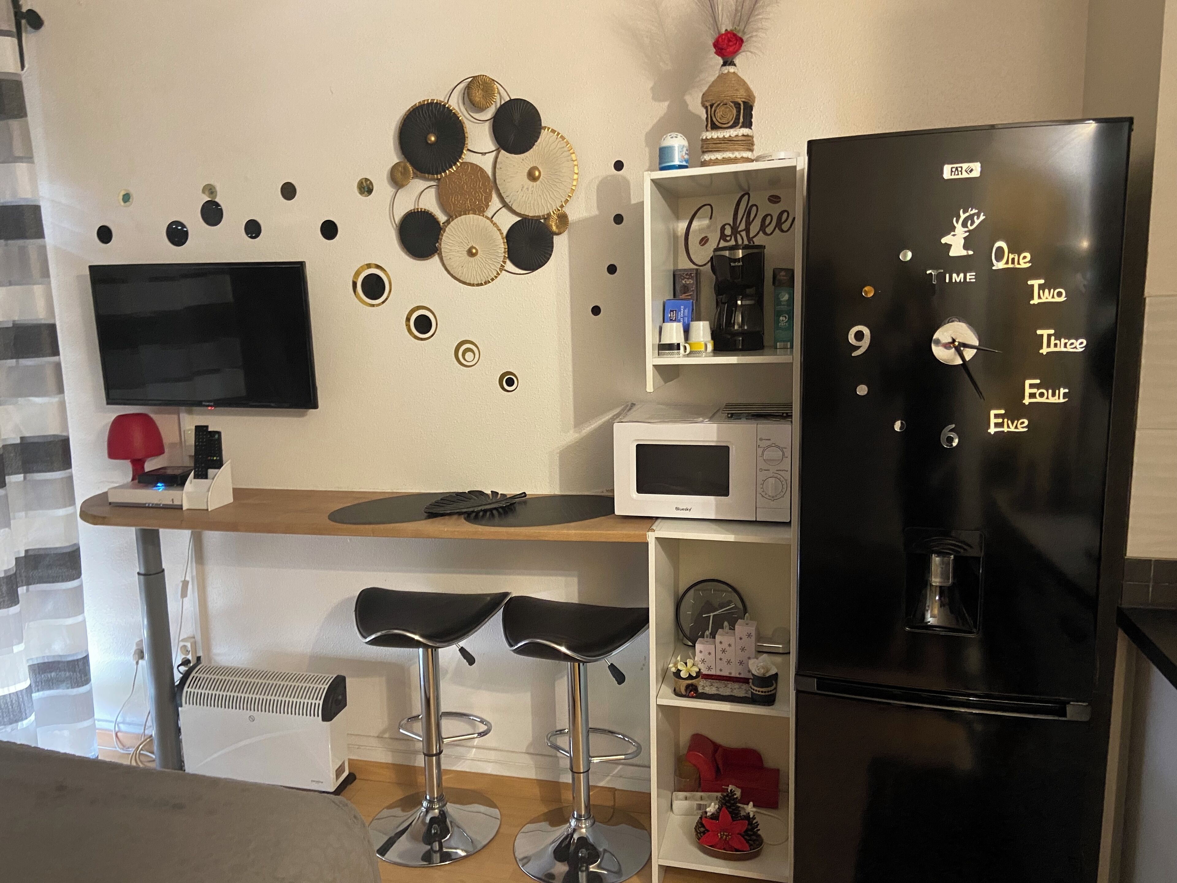 A modern kitchen with a black refrigerator, a microwave, and two bar stools.