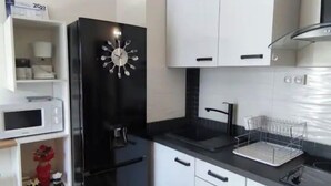 Une cuisine moderne avec des meubles blancs, un réfrigérateur noir, un four à micro-ondes et un four noir.