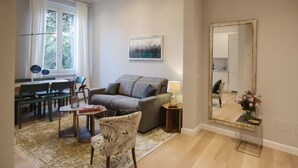 A living room with a grey sofa, a dining table with chairs, a large mirror, and a window with curtains. - Apartments Florence Oblate Exclusive (Florence)