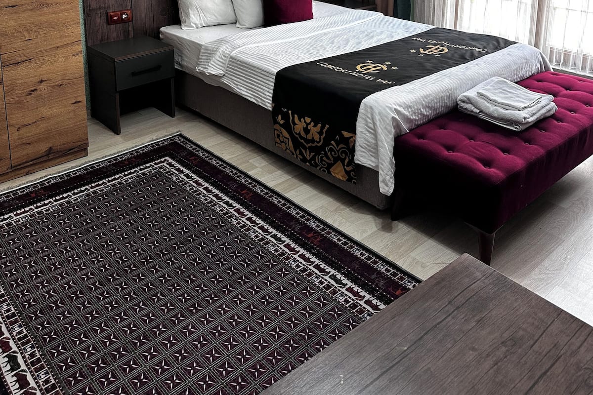 A bedroom with a large bed, a nightstand, a wooden wardrobe, a painting, and a chandelier.