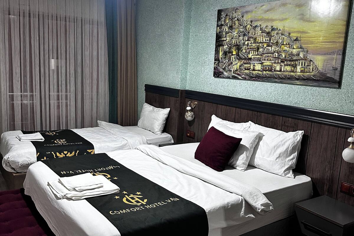 A hotel room with two beds, a large painting on the wall, and a nightstand.