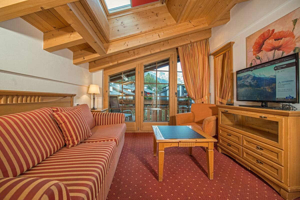 A cozy room with a wooden ceiling, a sofa, a table, a TV, and a window with curtains.