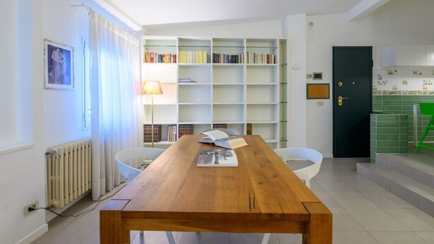 A modern living room with a wooden coffee table, white chairs, a bookshelf, and a green door. - Apartments Florence - San Lorenzo Market (Florence)