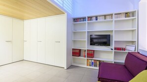 A modern living room with a flat-screen TV, white shelving with books, a purple sofa, and a large window. - Apartments Florence - San Lorenzo Market (Florence)