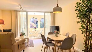 Una sala de estar moderna con sofá, mesa de comedor, sillas, televisor y un ventanal con cortinas.