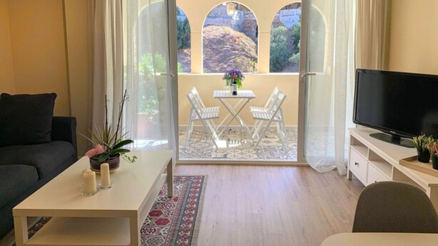 Una habitación con sofá, una mesita con velas, televisión y balcón con mesa y sillas.