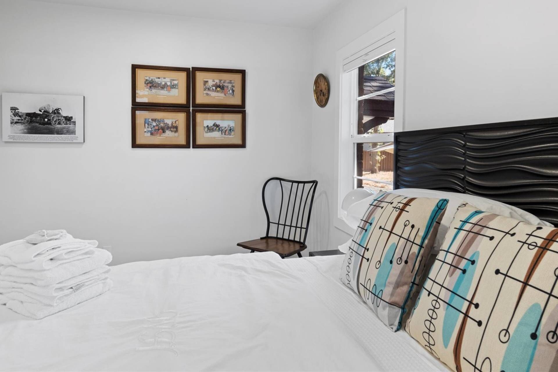 A bedroom with a bed, a chair, a window, and four framed pictures on the wall.