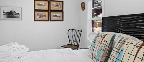 A bedroom with a bed, a chair, a window, and four framed pictures on the wall.