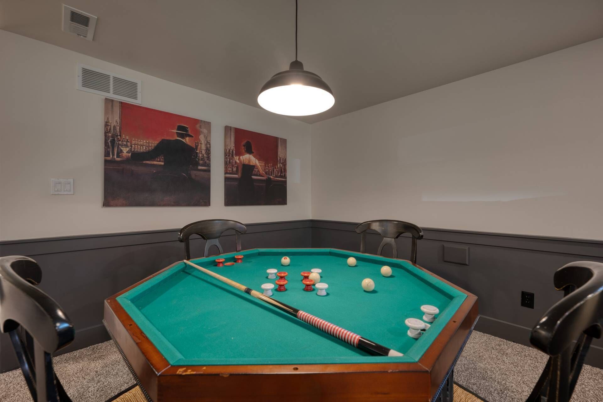 A pool table with balls and cues, four chairs, and two paintings on the wall.