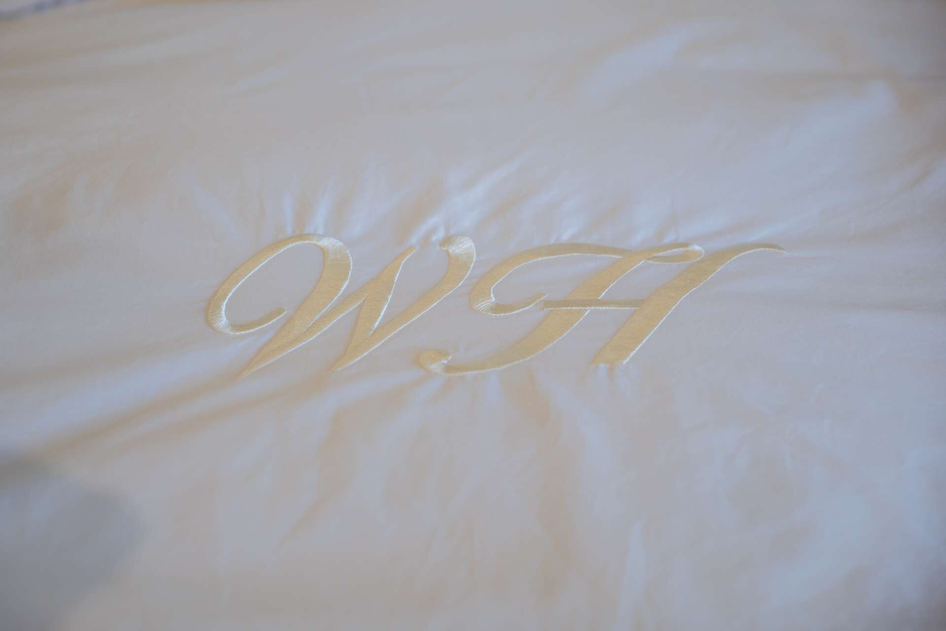 A bed with a monogram embroidered in gold on the white sheet.