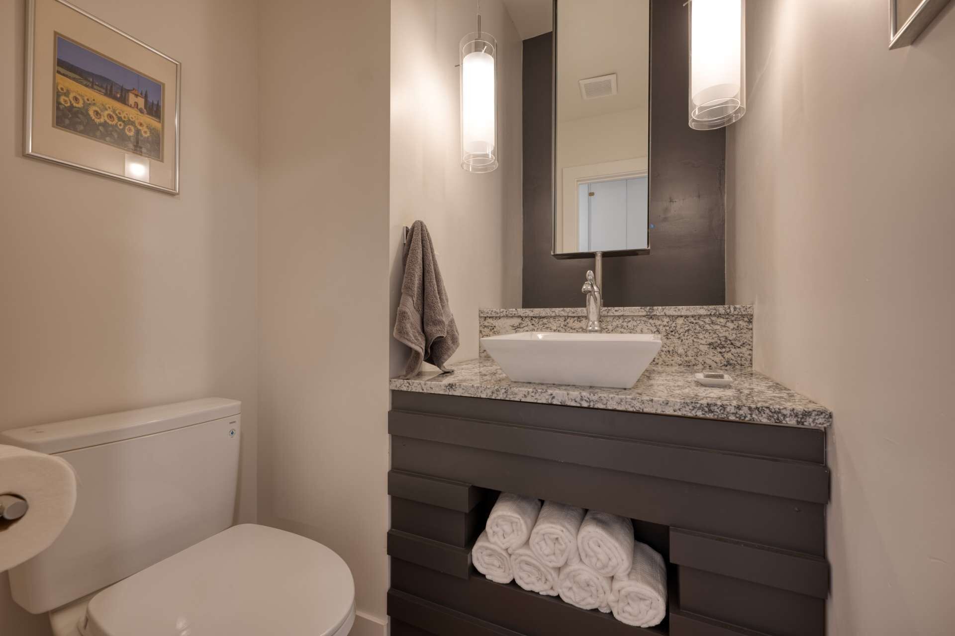 A bathroom with a white toilet, a sink with a marble countertop, a towel rack, and a mirror.