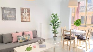Een moderne woonkamer met een grijze bank, een witte salontafel, een eettafel met stoelen en twee kunstwerken aan de muur.