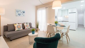 Una sala de estar moderna con un sofá gris, un sillón verde y un comedor con sillas blancas y una mesa.