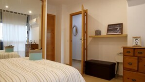 Una camera da letto con un letto, un comò, una panca piccola, una porta e una mensola con delle foto.