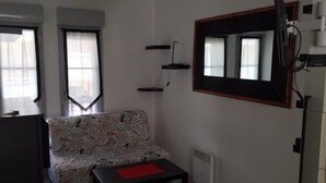 Une petite pièce, peu meublée, avec un seul canapé, une petite table, un téléviseur fixé au mur et un radiateur.