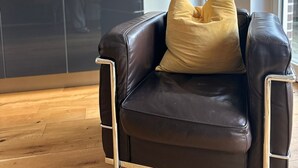 A modern living room with a black leather sofa, a single gold-colored cushion, and a wooden floor. - Entire accommodation "Historisches Nottuln", Baumberge - near Münster (Nottuln)