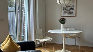 A modern living room with a black leather sofa, a white round dining table with chairs, a white vase with flowers, and a framed picture on the wall. - Entire accommodation "Historisches Nottuln", Baumberge - near Münster (Nottuln)