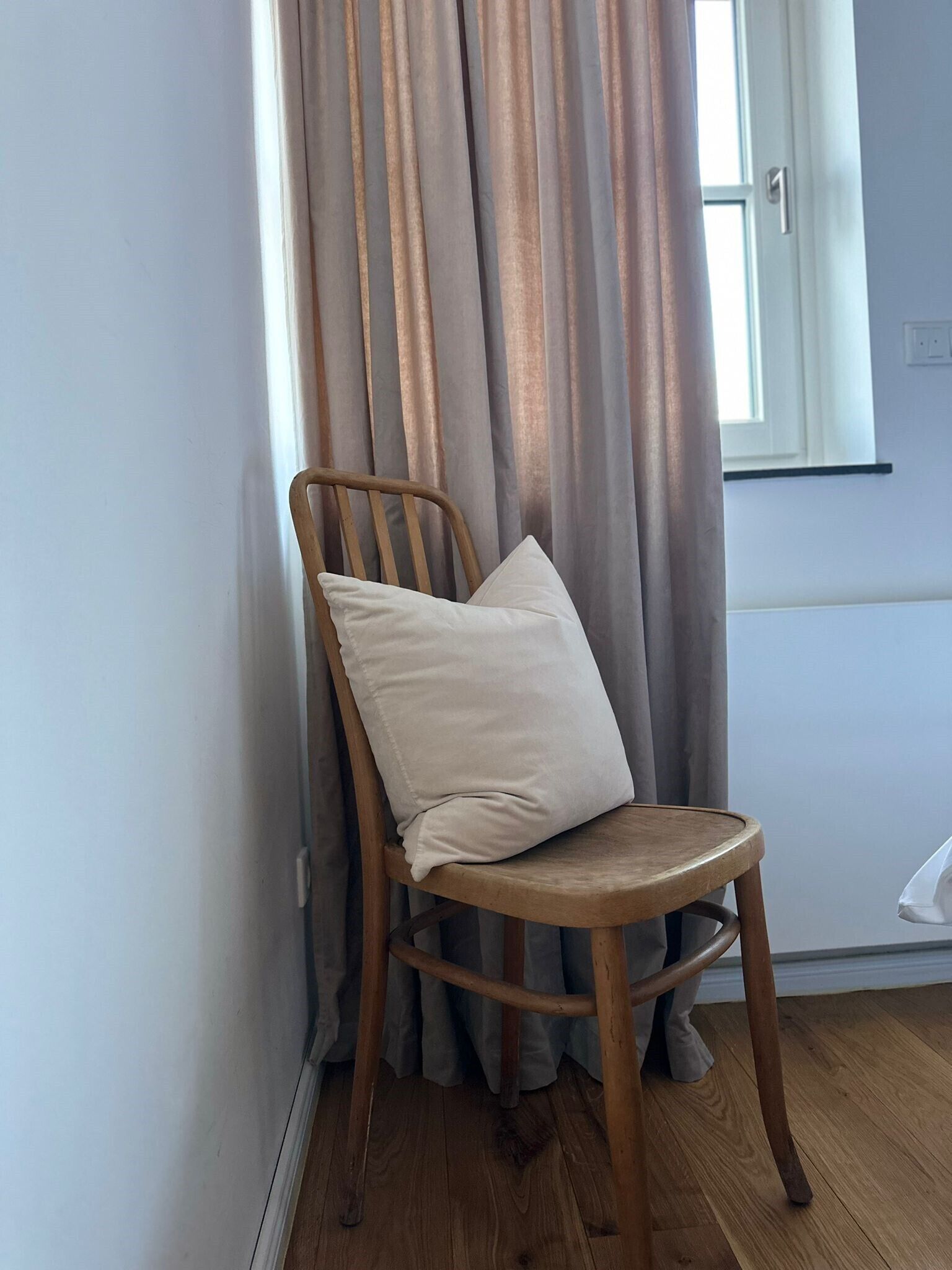 Een houten stoel met een kussen in een kamer met een raam en gordijnen.