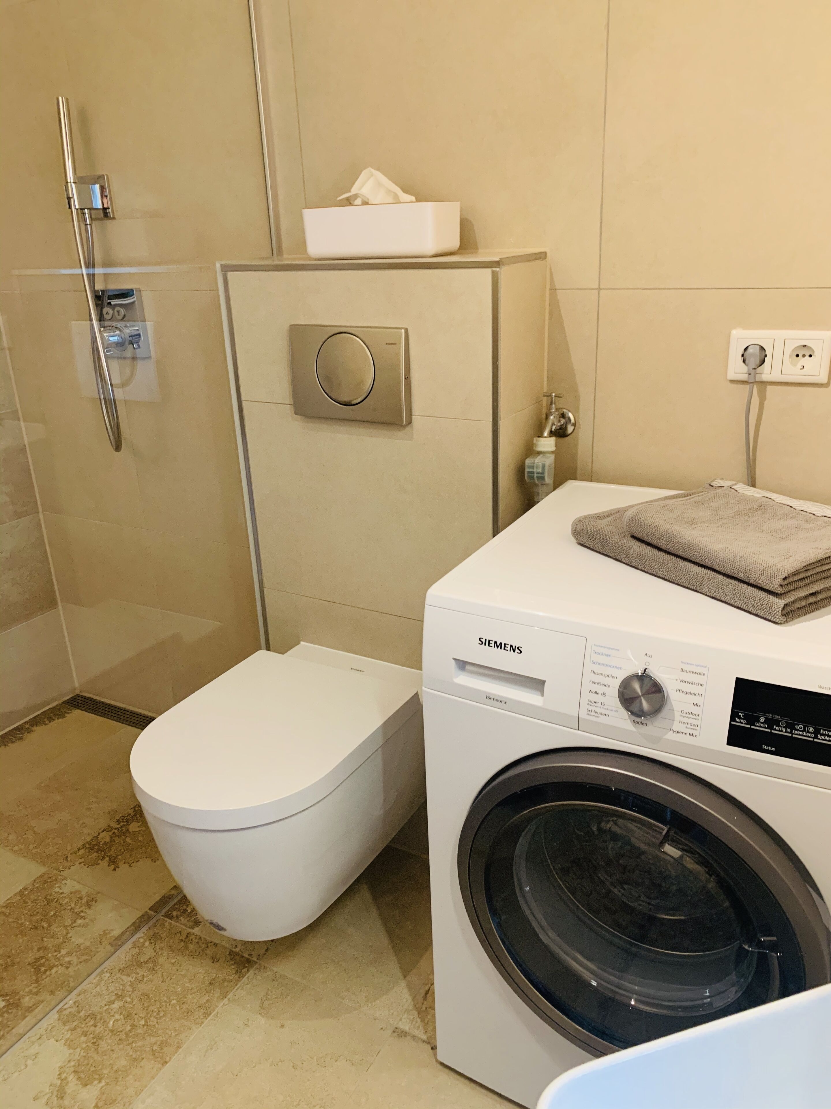 A modern bathroom with a toilet, a washing machine, and a shower.
